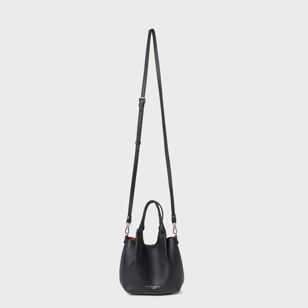 Bossa de mà Gianni Chiarini Dua XS de pell negra. Té un mànec curt i una corretja de bandolera de longitud ajustable, dret sobre un fons gris clar llis.