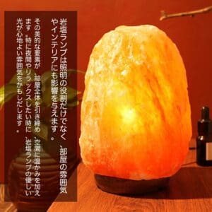 A 天然岩塩ランプ【サイズ：SS】— ほっと落ち着く、優しい間接照明が、ダークウッドの台座の上で柔らかく輝き、天然の結晶を通して温かみのあるオレンジがかったピンク色の光を放っています。左側に配置された日本語の文字と小さな植物が、この居心地の良い穏やかな情景をさらに引き立てています。.