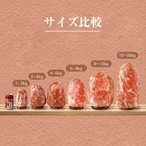 Seven 天然岩塩ランプ【サイズ：SS】—ほっと落ち着く、やさしい間接照明。さまざまなサイズのモデルが、大きさを比較するためにソーダ缶と一緒に並べられています。 ヒマラヤ岩塩で作られた各ランプには、1～2kgから12～20kgまでの重量範囲がラベルに記載されており、間接照明に最適です。上部には、質感のある背景に日本語のテキストが記載されています。.