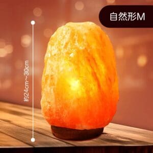 天然岩塩ランプ【サイズ：SS】— ほっと落ち着く、優しい間接照明。木製の台座の上に置かれ、間接照明として柔らかなオレンジ色の光を放っています。高さ約24～30cmと表示され、右上隅には日本語の文字が記されたこの天然岩塩ランプは、どんな空間にも温かみと安らぎをもたらします。.